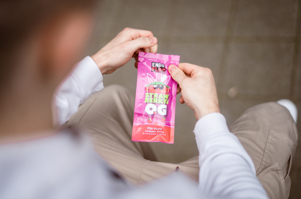 Man sat whilst opening the pouch of a Strawberry OG EndoFlo CBD vape pen